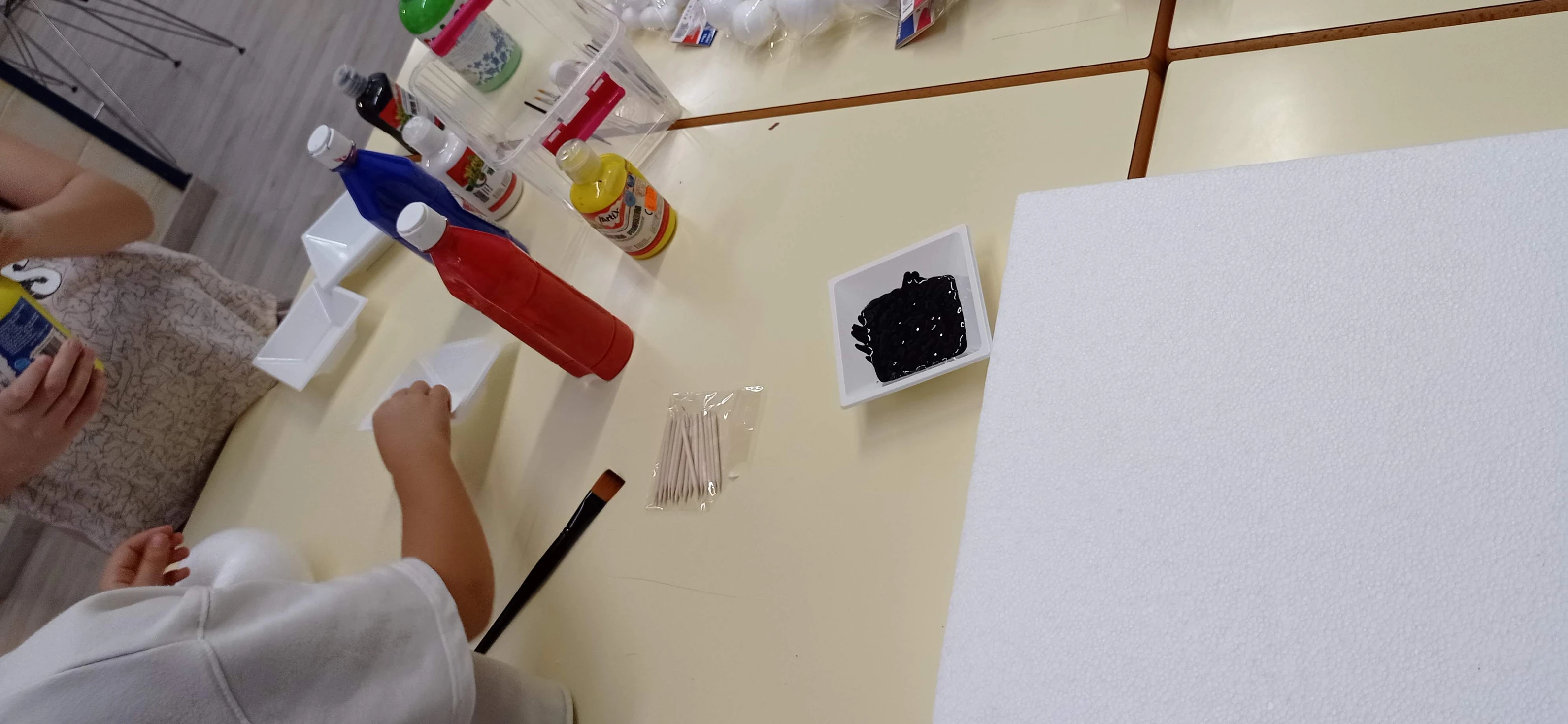 Mesa llena de botes de pintura y objetos de manualidades